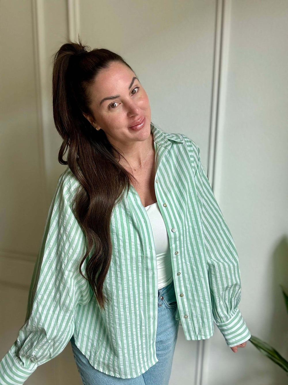 Woman wearing a green and white striped button down shirt with balloon sleeves, showcasing effortless style.