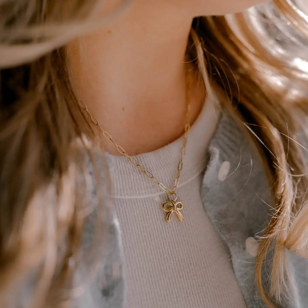 Close-up of a woman wearing a gold bow charm necklace, symbolizing faith and connection.