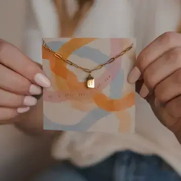 Woman holding With You Mini Tag Necklace on a colorful card, emphasizing God's promises from Isaiah 41:10.