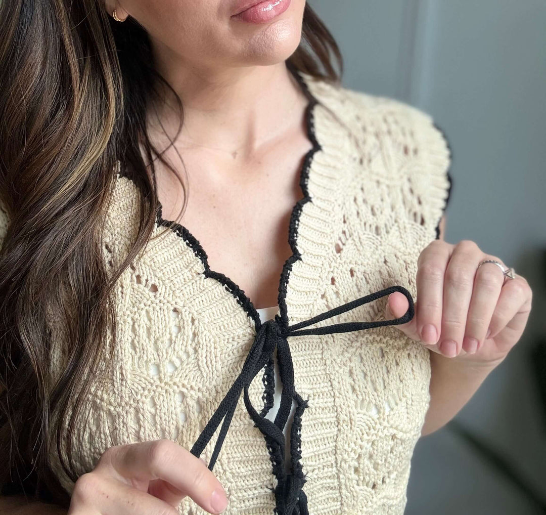 Close-up of a woman tying the bow on a Faithful Threads crochet sweater vest with scallop edges.