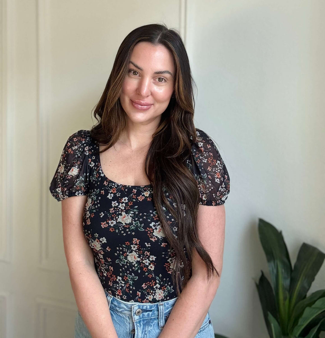 Young woman wearing a Floral Breeze Bodysuit with black background and floral pattern, showcasing style and comfort.