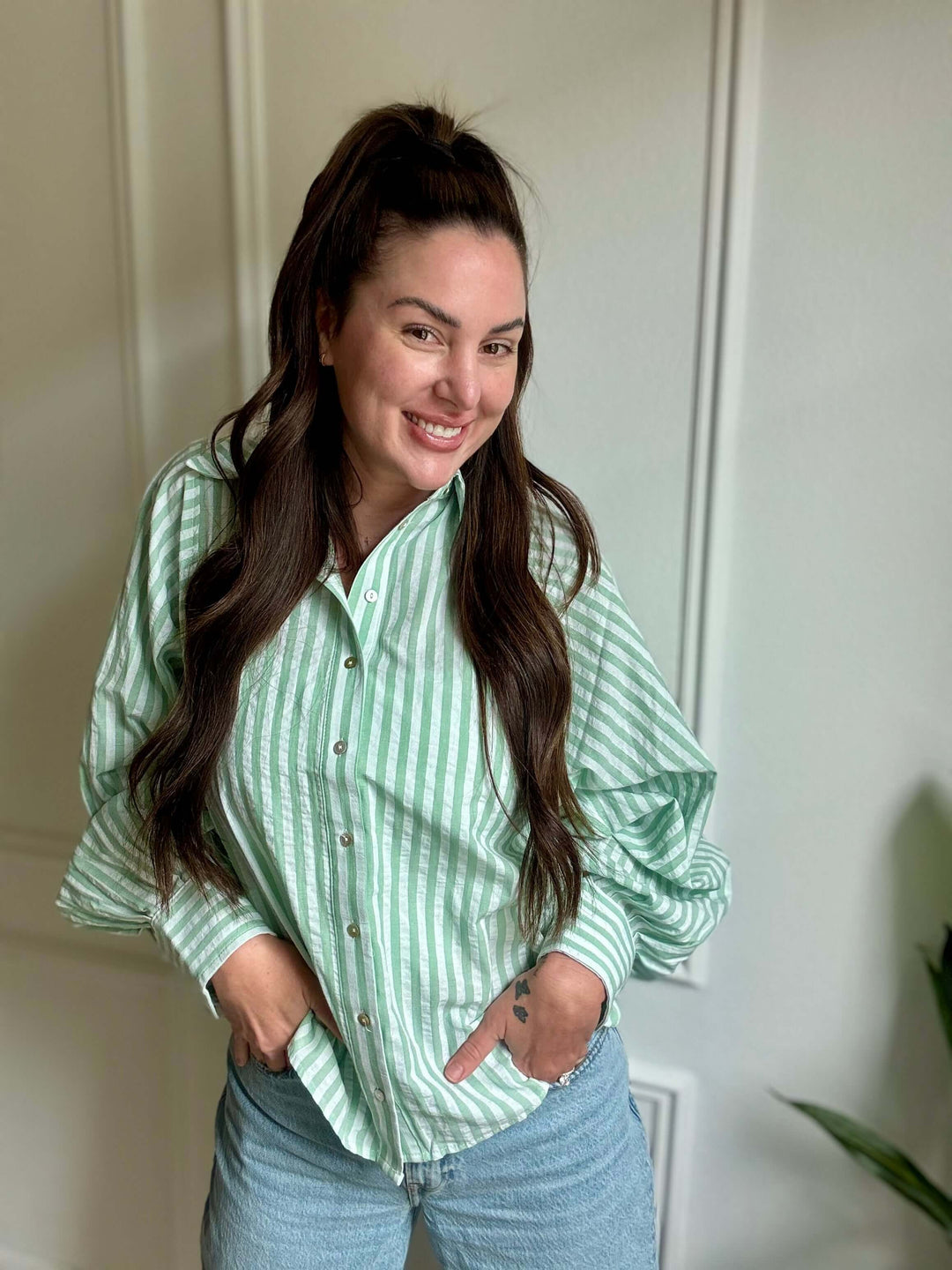 Smiling woman wearing a green and white striped button-down shirt, embodying casual elegance.