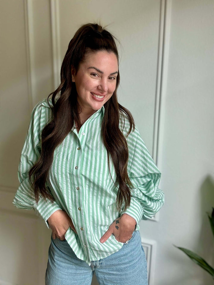 Smiling woman wearing a green and white striped button-down shirt, embodying casual elegance.
