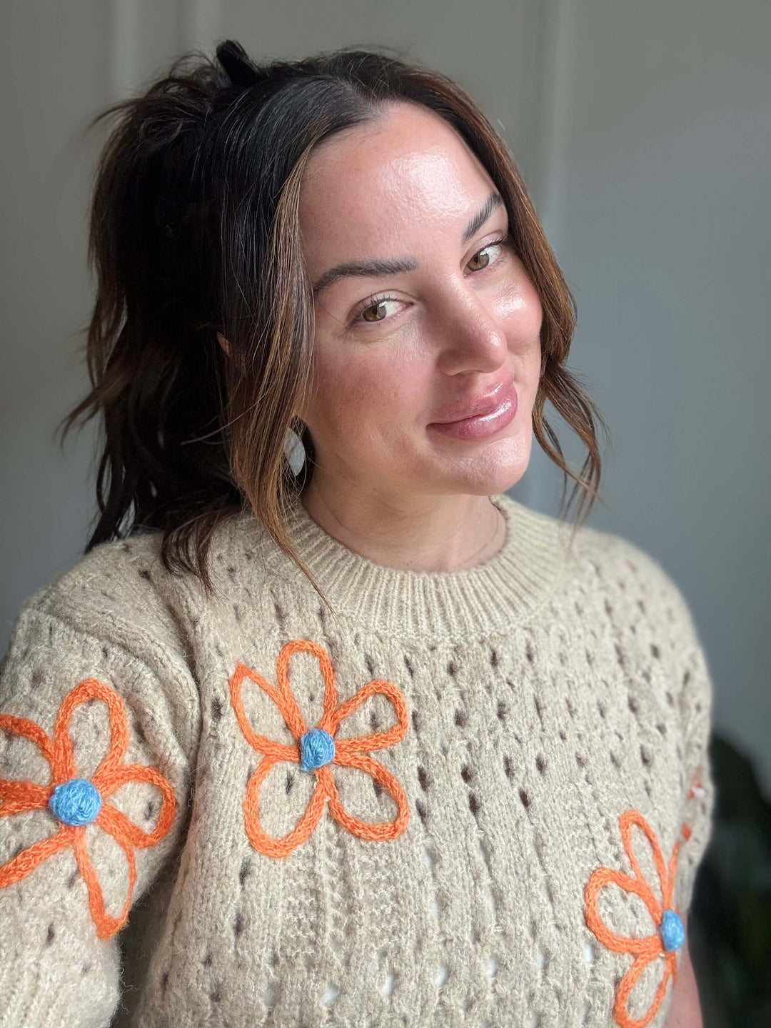 Woman smiling while wearing a floral knit sweater, showcasing its delicate orange and blue embroidery.