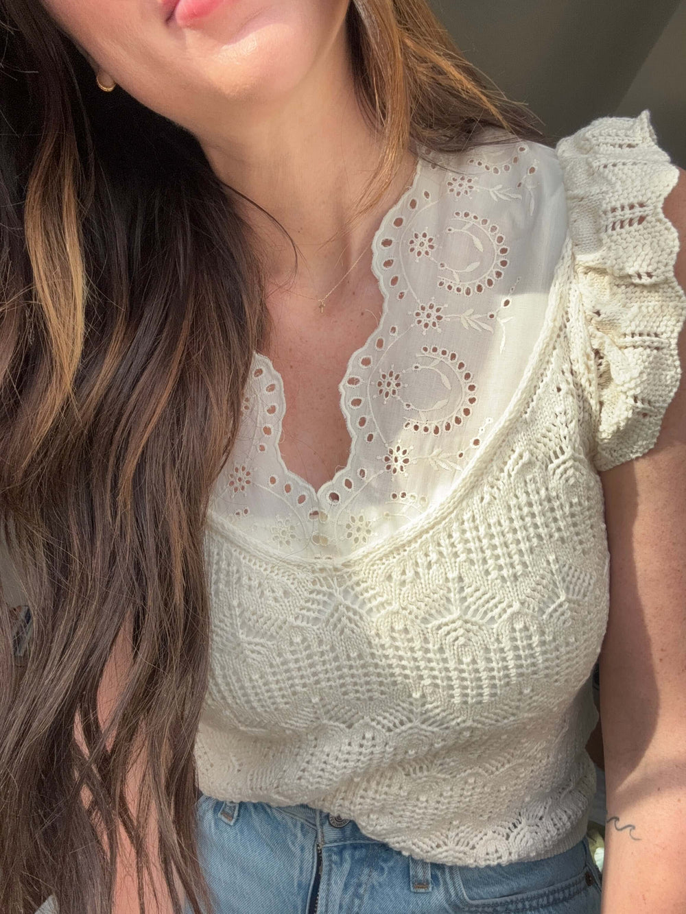 Close-up of a woman wearing a white lace patchwork top with ruffled sleeves, showcasing elegance and style.