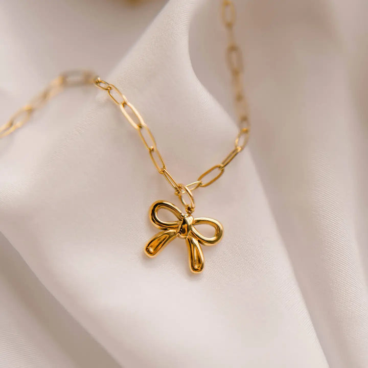 Gold bow charm necklace on a delicate chain, symbolizing hope and faith from Colossians 1:17.