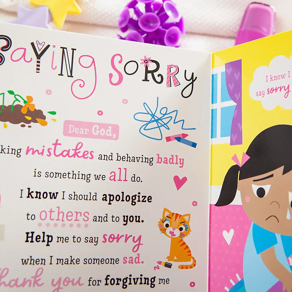 Open page of 'My Pretty Pink Prayer Book for Kids' showing a prayer about saying sorry with colorful illustrations.
