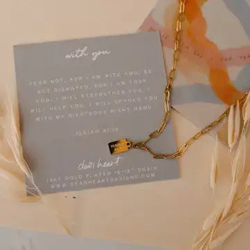 With You Mini Tag Necklace featuring gold pendant, inspirational card with Isaiah 41:10, styled with natural elements.